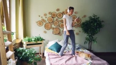 Modern Afro-Amerikan kız akıllı çalma listesi ve güzel daire yatakta dans parça seçme kulaklık aracılığıyla müzik dinlemek.