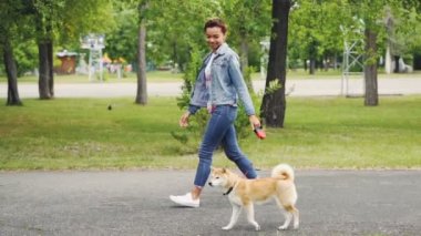 Ağır çekim yan görüntülemek doğanın keyfini ve etrafa Şehir Parkı safkan köpek yürüyüş güzel kız. Sağlıklı yaşam tarzı, evde beslenen hayvan mülkiyet ve neşeli gençlik kavramı.