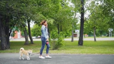 Mutlu karışık yarış kız yürüyen köpek park ve arkadaş arama cep telefonda konuşurken ağır çekim. Modern teknoloji, sevgi dolu hayvanlar ve iletişim kavramı.