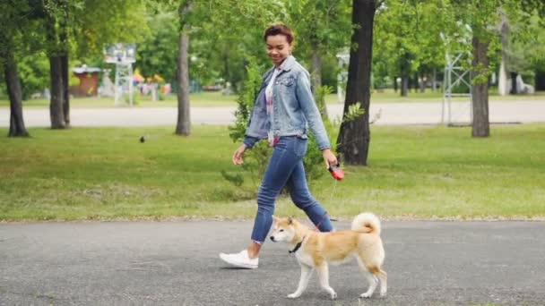 Zeitlupe Seitenansicht eines hübschen Mädchens, das reinrassige Hunde im Stadtpark spazieren führt, die Natur genießt und sich umsieht. Gesunder Lebensstil, Haustierbesitzer und fröhliches Jugendkonzept. — Stockvideo