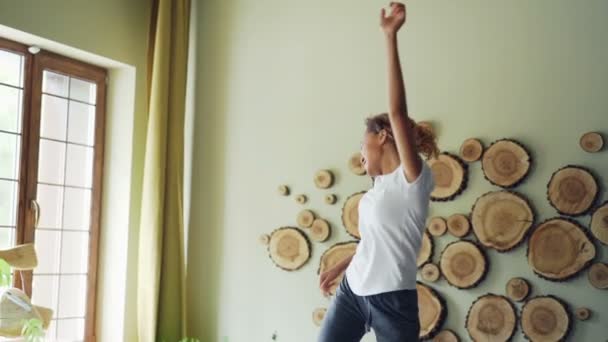 Slow motion van vrolijke Afro-Amerikaanse tiener luisteren naar muziek, dansen en zingen op bed in de slaapkamer, terwijl gezelschapsdier is rust. Plezier en dieren concept. — Stockvideo