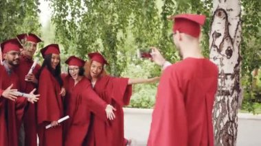 Mezun olan öğrenci diploma holding, el sallayarak ve smartphone kameraya bakarak poz önlük içinde arkadaşları video kaydediyor. İnsan ve teknoloji kavramı.