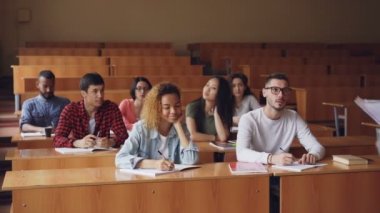 Grup öğrenci öğretmen için dinleme ve Profesör konuşurken ve mimik masalarda oturma sınıfta yazma. Yüksek öğrenim ve insanlar kavramı.
