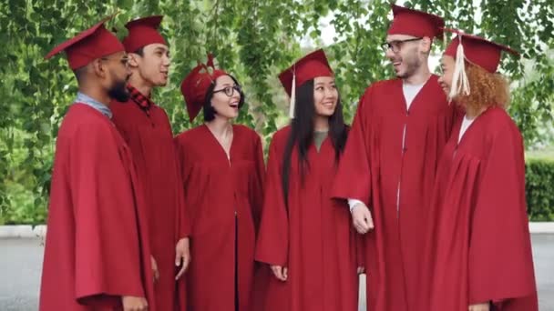 Estudantes de graduação feliz grupo multiétnico está colocando palmas juntas, em seguida, batendo palmas celebrando a formatura bem sucedida, as pessoas estão vestindo vestidos e almofadas . — Vídeo de Stock