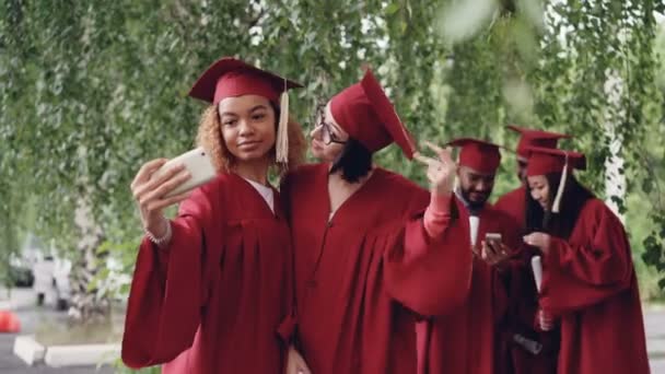 Vackra unga kvinnor examen studenter tar selfie med smartphone då titta på fotografier. Modern teknik, millennials och utbildning koncept. — Stockvideo