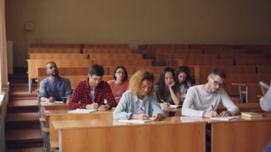 Profesör grup raporları ile sınıfta ayakta ve gençler için onu dinlerken konuşma ve yazma çalışma masaları, oturma çok ırklı öğrenci için ders okuma.
