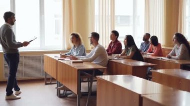 Dost öğretmen gençler elleri yükseltmektedirler iken soru sorma ve cevaplamanın masaları, oturma öğrencilere konuşuyor. Yüksek okul, eğitim ve gençlik kavramı.