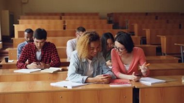 Neşeli öğrenciler akıllı telefonlar kullanarak ve Üniversitesi'nde dersler arasında mola sırasında sohbet. Modern teknoloji, gençlik ve eğitim kavramı.