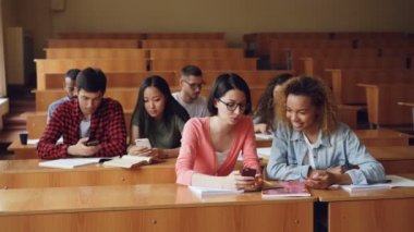 Gençlerin akıllı telefonlar kullanarak ve oturma sıraları Üniversitesi'nde konferans salonunda, söz. Ahşap mobilyalar, kadınlar ve erkekler ile geniş oda, dizüstü bilgisayarlar tarafından görülebilir.