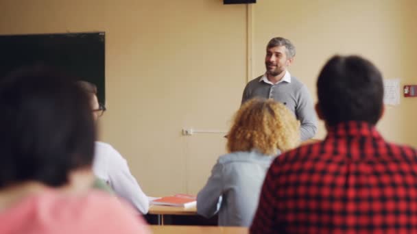 Der freundliche Lehrer spricht zu seinen Schülern, die ihr Wissen überprüfen, ein junger Mann hebt die Hand und beantwortet Fragen, andere Schüler hören zu. Lehr- und Lernkonzept. — Stockvideo