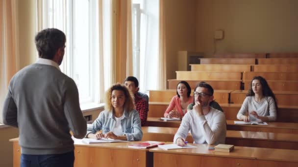 Grupo multiétnico de jóvenes está escuchando a la maestra y sonriendo luego levantando las manos, la maestra está apuntando a la chica asiática y hablando con ella. Concepto de alumnos y tutores . — Vídeos de Stock