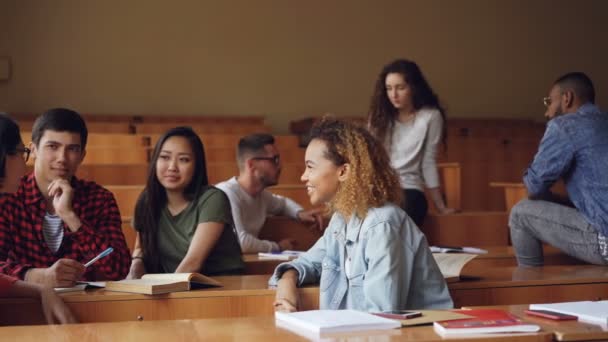 Hombres y mujeres jóvenes alegres se relajan durante el descanso en la universidad, los jóvenes están charlando, riendo y discutiendo el libro de texto. Concepto inteligente de juventud y educación . — Vídeos de Stock