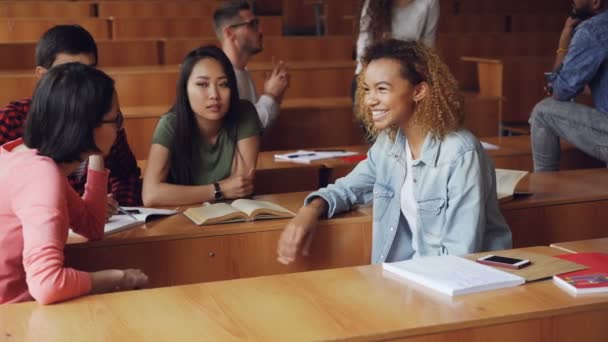 Unga kvinnor har konversation efter föreläsningar på college, flickor pratar och gestikulerande medan andra elever chattar i bakgrunden. Ung och kommunikation koncept. — Stockvideo