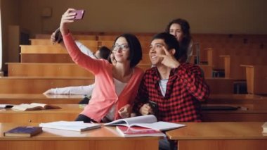 Neşeli öğrenciler selfie birlikte masaları oturma ve akıllı telefonlar holding konferans salonunda alıyor. Modern teknoloji, kendi portresi ve eğitim kavramı.