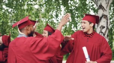 Heyecanlı genç kadın ve erkek mezunlar çak bir beşlik, kucaklayan ve holding diploma mezuniyet günü kutlayan gülerek yapıyoruz. Duygu ve başarı kavramı.
