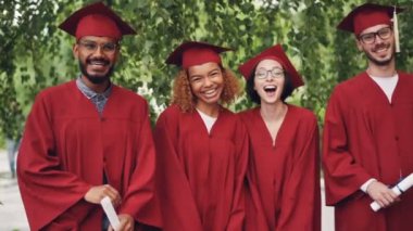 Dolly yavaş genç insanlar mutlu mezunları diploma açık havada kutlama zevk kampüste doğrultusunda ayakta tutan gülen vurdu. Mezuniyet günü ve gençlik kavramı.