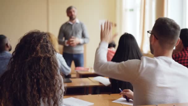 Συμμετέχοντα Διάσκεψη Νεολαίας νεαρού γυαλιά είναι αύξηση το χέρι και μιλώντας με δάσκαλο ενώ άλλοι άνθρωποι βλέπουν παιδαγωγός και ακούτε συνομιλία. — Αρχείο Βίντεο