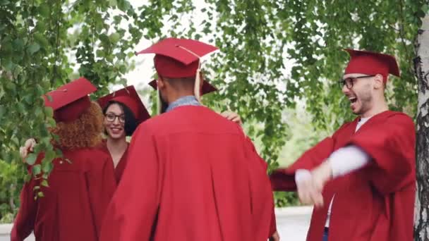 Önlük ve şapka neşeli kız ve erkek mezunlar mezuniyet üzerinde birbirlerini tebrik ediyor, gülen ve having fun sarılıyorlar. Yüksek öğrenim ve başarı kavramı. — Stok video