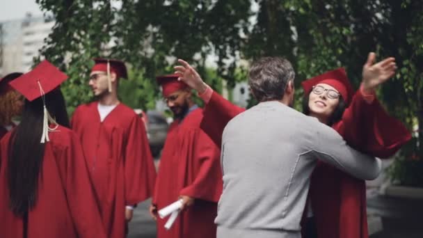 Stolt förälder kramar hans framgångsrika dotter examen står utomhus på campus och firar examen dag. Familj, utbildning och event koncept. — Stockvideo