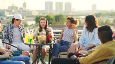 Pretty genç kız için yiyecek ve içecek, arka planda şehir görünümüdür güzel çatı masada oturan arkadaşlar çok ırklı grubu hikaye anlatıyor.