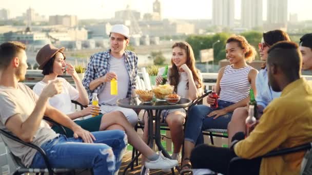 Boldog lányok és a fiúk a diákok, amelyek tetőtéri party pirítás és fogyasztói élvezi a szabad idő nyáron. Beszélgetés, a fiatalok és az ünneplés koncepció. — Stock videók