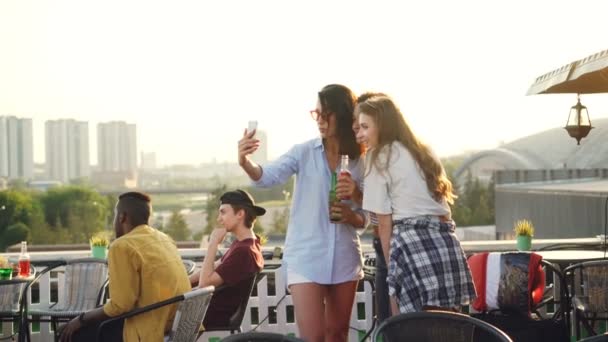 Amies gaies prennent selfie avec smartphone et rire debout sur le toit avec des boissons dans des bouteilles profiter de la fête. Concept de technologie, boissons et jeunesse . — Video