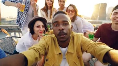 Gülümseyen ve şişe komik çatı partisi ile poz fotoğraf makinesi, Afro-Amerikan yakışıklı selfie mutlu arkadaşlarıyla insanlar alarak bakış açısı shot bakıyorsun.