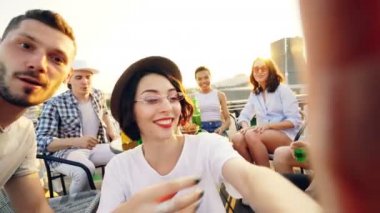 İnsanlar kamera ve alma selfie çatı eğleniyor alkolsüz içecekler ile arkadaş grubu holding trendy şapkalı güzel Bayan bakış açısı shot kameraya bakıyor ve gülüyor.