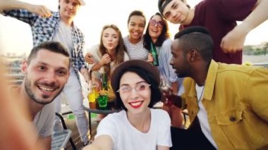 Genç kadın kamera tutarak ve arkadaşları poz ve açık havada partide el hareketleri gösteren gözlük, tungur iken kameraya bakarak selfie alma.