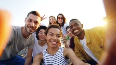 Bakış açısı shot kamera tutarak ve çatıda partide mutlu arkadaş grubu selfie alarak Afrikalı-Amerikalı kız. Kadın ve erkek kameraya bakarak, poz ve gülüyor.