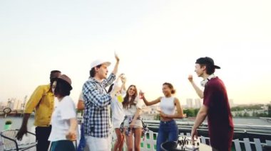 Neşeli Dj karıştırma konsol ve genç adam çatıda modern partide dans için söz ile çalışıyor. Kadın ve erkek moda giysiler giyen ve şişeler tutan.