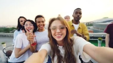 Bakış açısı shot genç ve güzel kadın kayıt video çatı katındaki dans ve kameraya bakarak arkadaşları ile parti. Eğlence, gençlik ve müzik konsepti.