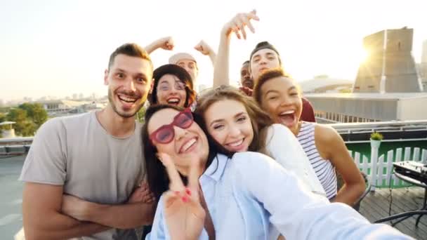 여름 파티, 포즈 웃으면서 즐기는 좋은 회사에서 지붕에 selfe를 복용 하는 행복 한 친구의 관점 샷. 행복, 레저 및 기술 개념. — 비디오