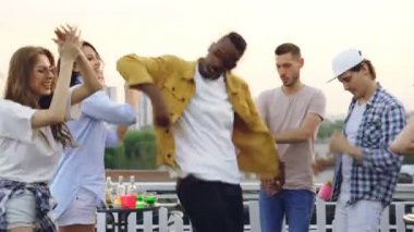 Trendy kıyafetler içinde neşeli Afro-Amerikan erkek arkadaş çok ırklı grup yaz gününde çatıda partide eğleniyor ile dans ediyor. Boş zaman, sevinç ve dostluk kavramı.