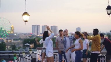 Arkadaşlar çok ırklı grup cool Dj ile yaz aylarında akşam parti çatı üzerinde dans ediyor. Neşeli gençlik, eğlence ve büyük şehir kavramı.