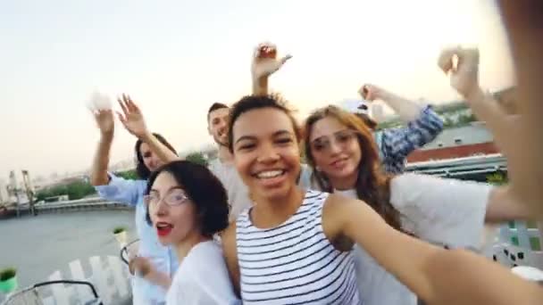 Jóvenes y alegres amigos y amigas están bailando levantando las manos y divirtiéndose en la fiesta en el techo en verano. Estilo de vida moderno, amistad, ocio y concepto musical . — Vídeo de stock