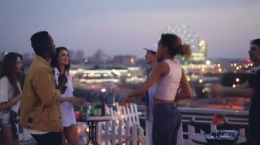 Neşeli genç insanlar dans ve deejay neşeli genç adam Mikser donanımları ile çalışan ve kablosuz kulaklık kullanarak gülüyor çatıda parti veriyor.