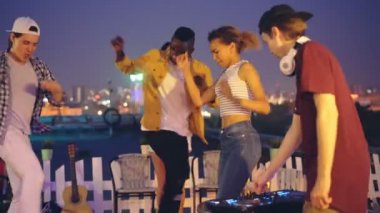 Neşeli erkek DJ karıştırma konsol ve arkadaşlar beyaz grup ve Afrikalı-Amerikalı çatı partide eğleniyor musun iken dans ile çalışma.