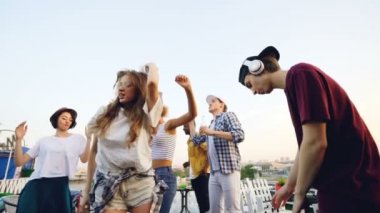 Ağır çekim Genç ve güzel kadın profesyonel ekipman deejay kablosuz kulaklık kullanırken çatı katında onun arkadaşlarıyla dans güneş gözlüğü.