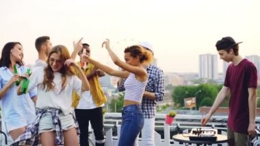 Yavaş genç kadın Dj profesyonel ekipman müzik yapma kullanırken çatı dans ve holding şişelenmiş içecekler üzerinde parti ve gülen.