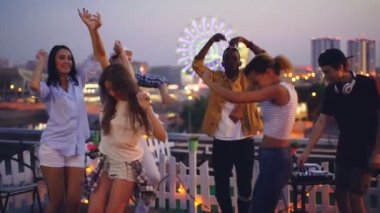 Ağır çekim neşeli insanlar kendilerini ve erkek deejay profesyonel ekipmanlarla modern müzik karıştırma zevk dans ile geç çatı partisi.