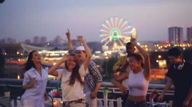 Ağır çekim çekici genç erkek ve kadınların rahatlatıcı ve having fun ile gülüyor, eller alkışlar ve karıştırma konsolu kullanarak yakışıklı deejay çatı üzerinde dans.