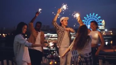 Yavaş hareket heyecan insanların gece çatı partide bengal ışıkları yanan ve birlikte eğlenmek ile dans. Eğlence, arkadaşlık, büyük şehir ve sevinç kavramı.