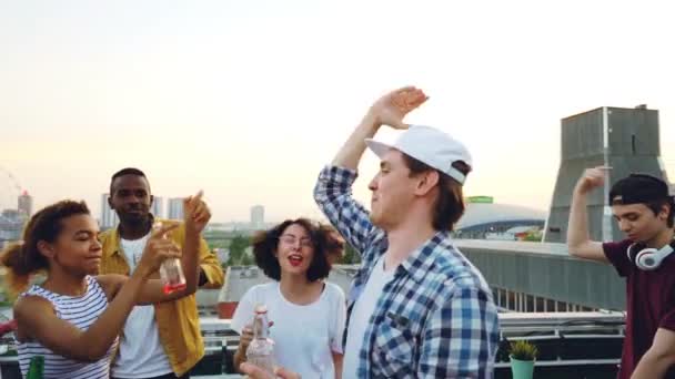 Movimento lento de jovens felizes dançando na festa ao ar livre no telhado se divertindo e relaxando no fim de semana segurando garrafas. Estilo de vida moderno, bebida e conceito de festa . — Vídeo de Stock