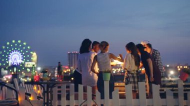 Ağır çekim maytap aydınlatma o zaman bengal yanma ile eller yükselterek mutlu insanlar arkadaş çatı ile arka plan güzel şehirde gece partide ışıkları.