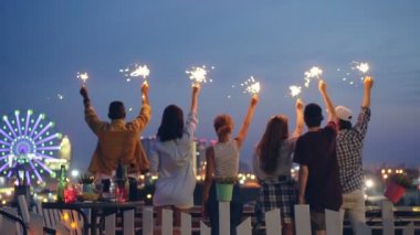 Yavaş yanan havai fişekleri ile sırtlarını çatıda kameraya yaz gecesi güzel şehirde ayakta tutan çekici gençlerin.