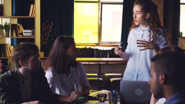 Female team leader is talking to her multiethnic team discussing business strategy in office of international company. Discussion, young people, workspace and planning concept. — Stock Video