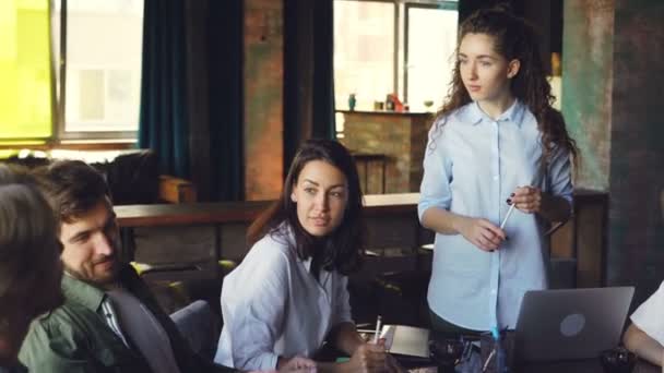 El equipo creativo de jóvenes profesionales está desarrollando una estrategia de trabajo durante la reunión de negocios en la oficina. Hombres y mujeres están sentados a la mesa y hablando . — Vídeo de stock