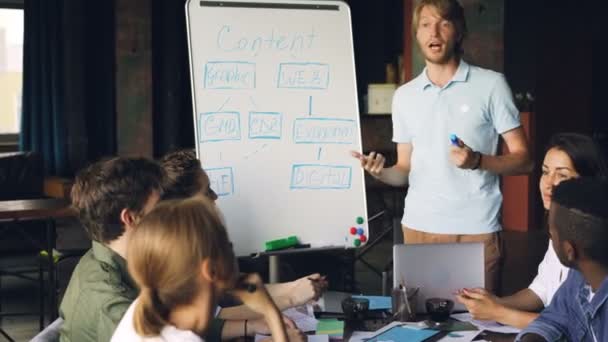 Emocional profesor de negocios está haciendo una presentación para estudiantes corporativos hablando y apuntando a pizarra blanca mientras los empleados de la empresa están escuchando y riendo . — Vídeo de stock