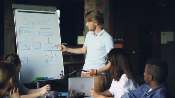 Team leader is making report at whiteboard talking and pointing at chart, team members are listening then clapping hands. Business, corporate education and people concept. — Stock Video